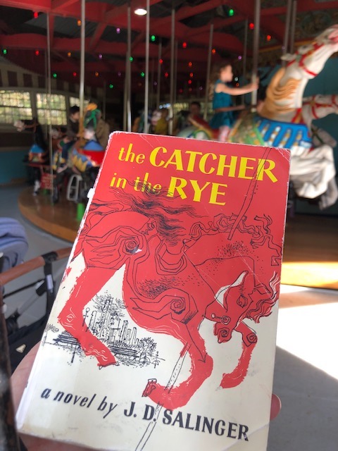 A copy of The Catcher in the Rye, in front of the Central Park Carousel