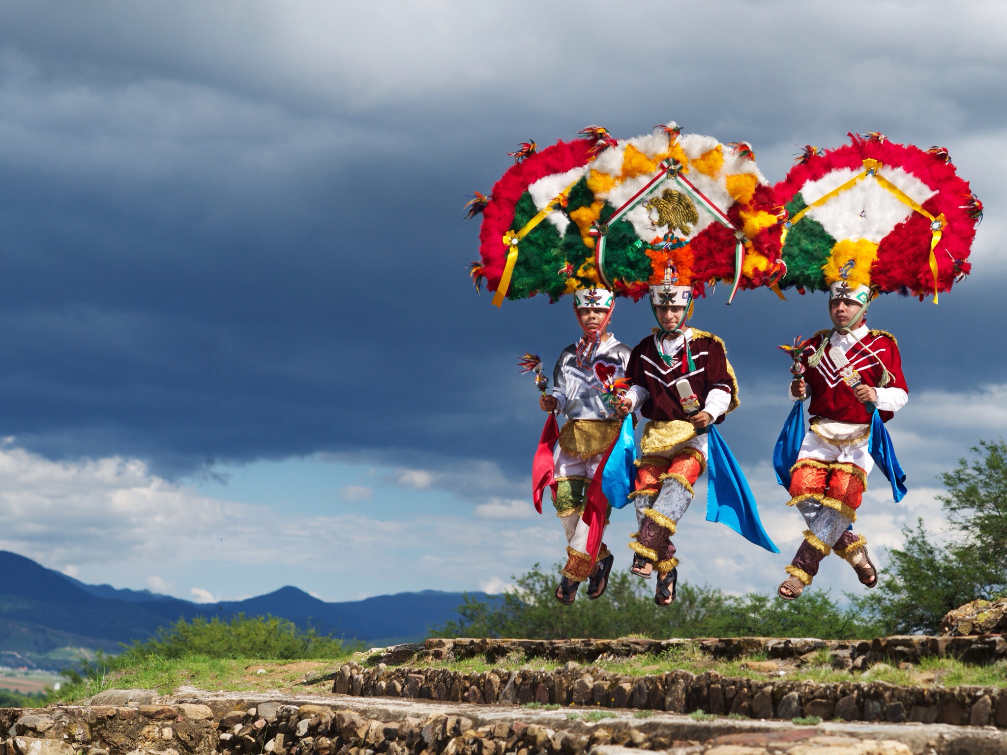 Three men wearing large feather headdresses dancing. 